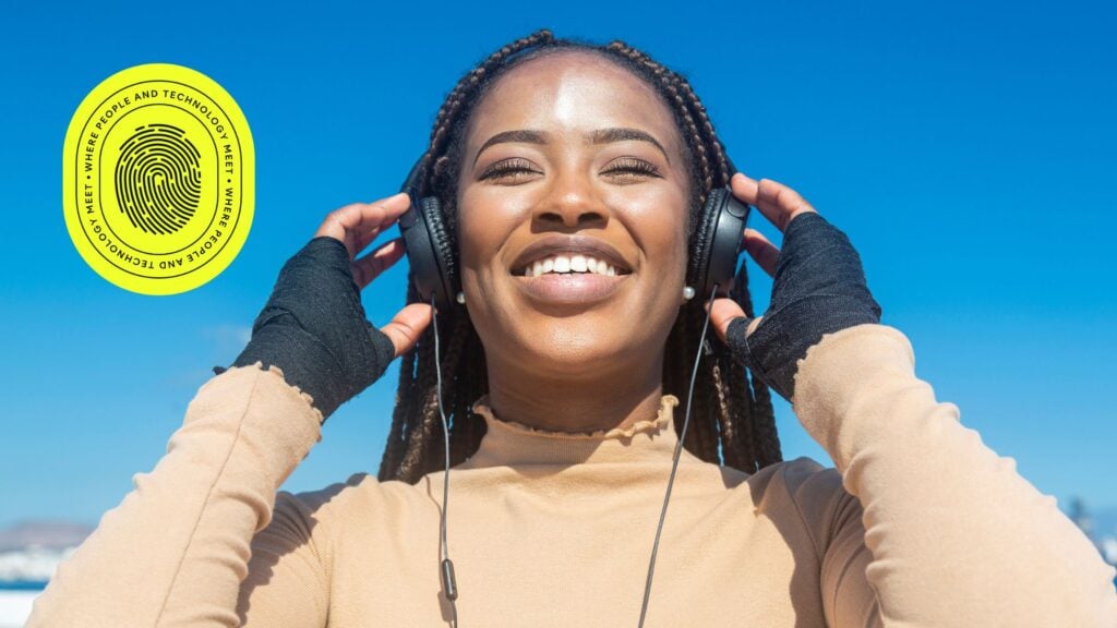 Smiling young woman with braids listening to music on headphones under a clear blue sky, symbolizing clarity and optimism—reflecting the SEO impact of changing domain names for a refreshed digital identity.